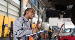 Female mechanic checking car engine underneath a car on a lift at auto car repair service. 