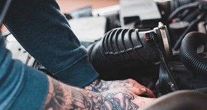 Tattooed vehicle technician fixing car engine considering changes in the industry and whether their job is at risk