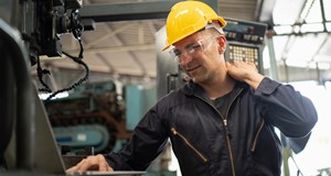 A person in a car manufacturing setting struggling with back pain.