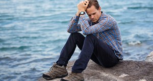 A person sitting next to the sea thinking and looking worried.