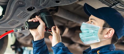 Mechanic wearing a face mask working on the underside of a car