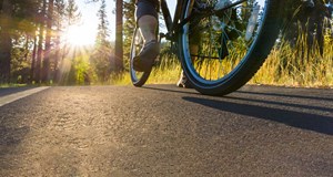 Cyclist riding down tarmac road through woodlands and forest