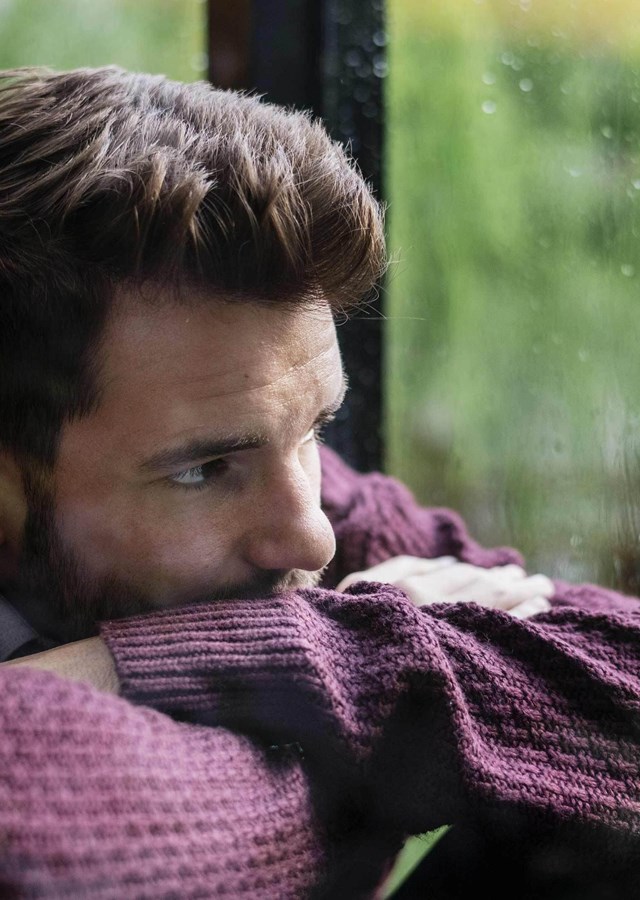 Person resting their chin on crossed arms looking out a window on a rainy day