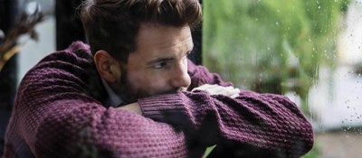 Person resting their chin on crossed arms looking out a window on a rainy day