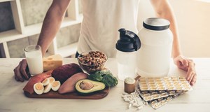 A person standing at a kitchen counter which has a variety of healthy nutritional foods on it to aid physical activity