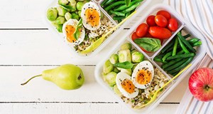 Two lunchboxes filled with colourful healthy foods ready to enjoy on the go. There is a red apple to one side of the boxes, and a green pear to the other.