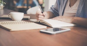 Person sitting with a hot drink, writing down notes in preparation for a job interview