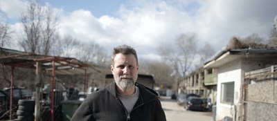 A person standing outside in a car scrap yard looking towards the camera.