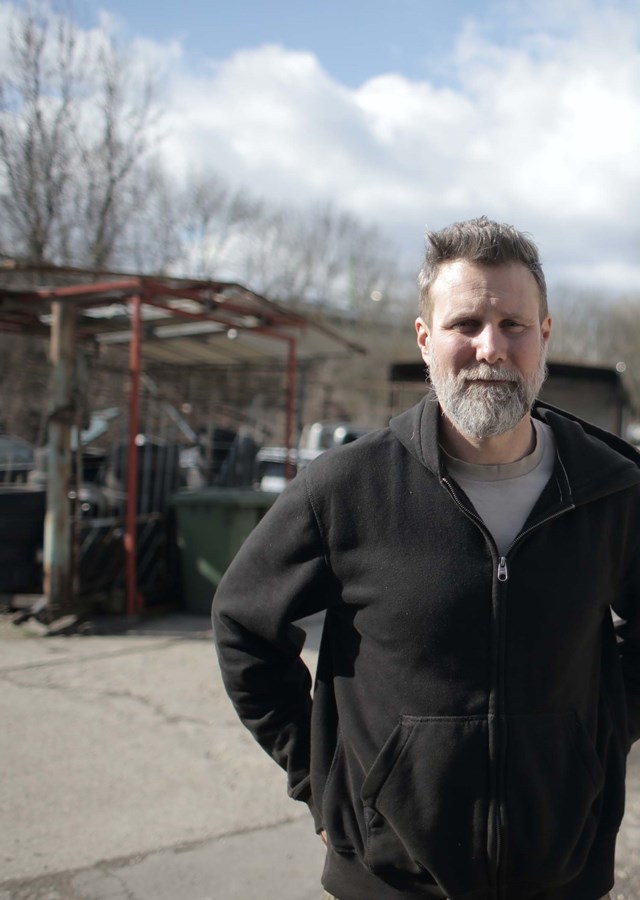 A person standing outside in a car scrap yard looking towards the camera.