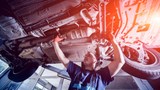 A smiling mechanic working on the underside of a car 