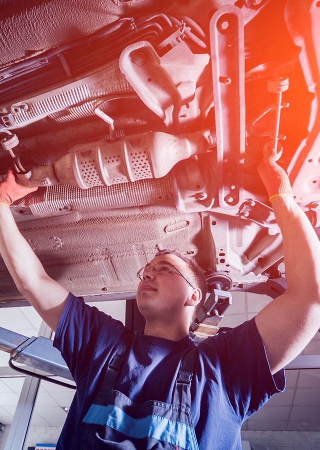 A smiling mechanic working on the underside of a car 