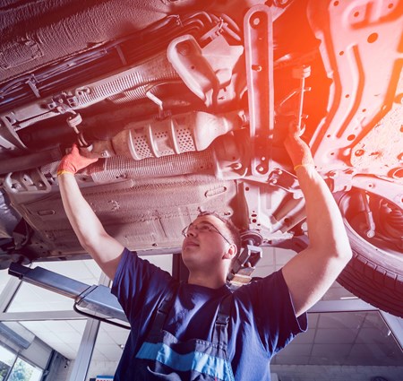 A smiling mechanic working on the underside of a car 