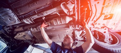 A smiling mechanic working on the underside of a car 