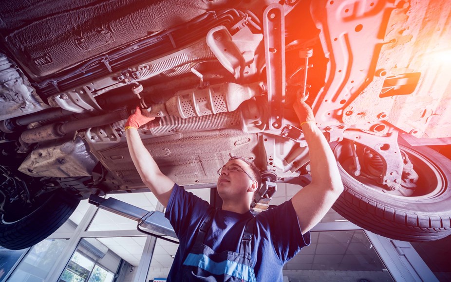 A smiling mechanic working on the underside of a car 