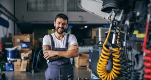 A smiling mechanic (vehicle technician) standing in a garage next to a truck being repaired