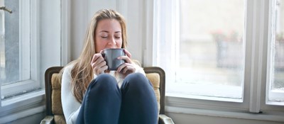A person enjoying a hot drink with their legs curled up on chair on a wet afternoon. 
