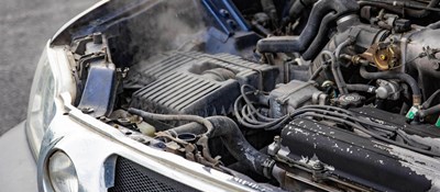 A car with its bonnet open showing the engine with smoke coming from the engine area