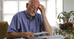 Person sat at a table with head in hands surrounded by bills looking worried about money