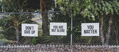 Three white signs, saying,' don't give up', 'you are not alone' and 'you matter', attached to a metal fence