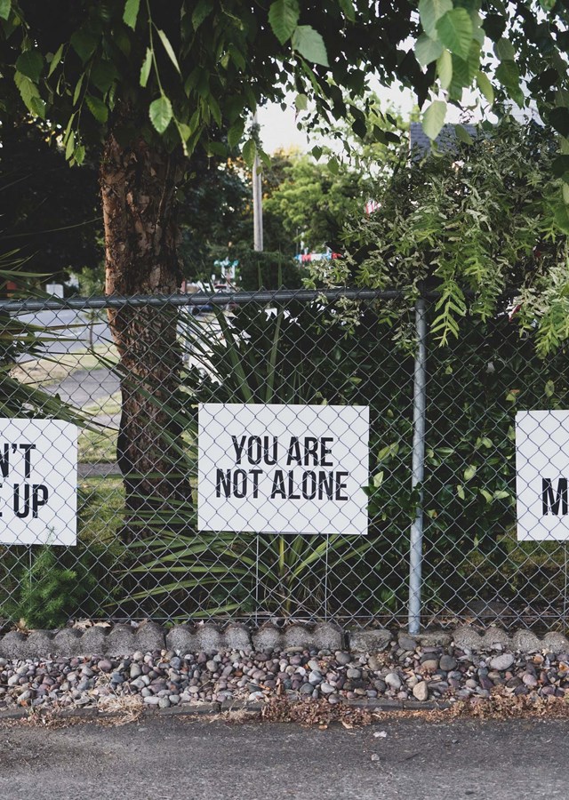 Three white signs, saying,' don't give up', 'you are not alone' and 'you matter', attached to a metal fence