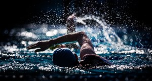 Swimmers, swimming through lanes wearing swimming caps  