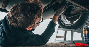 A mechanic (vehicle technician) lying on the floor working on the under side of a car