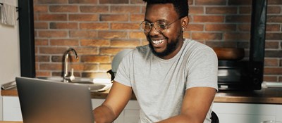 Happy man working from home in his kitchen using a laptop. There are benefits and challenges for working from home